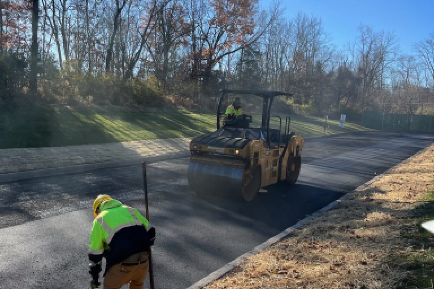 Vibratory roller compacting a fresh asphalt mat on a commercial road with a Beckage crew member in NJ