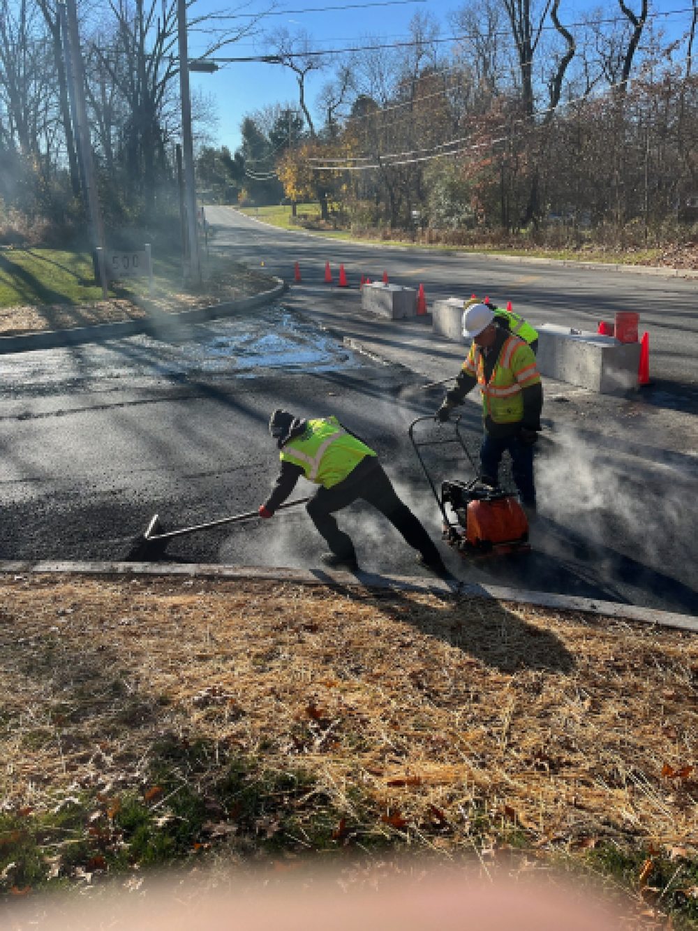 Beckage crew raking and plate-compacting hot asphalt at a commercial road entrance in NJ