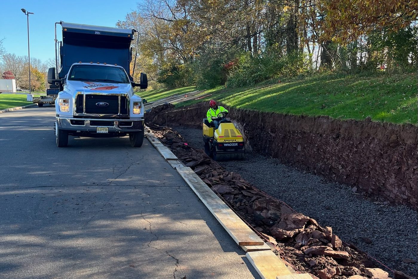 Beckage Sealcoating dump truck on site while a crew compacts the stone base for a new curb line along a parking lot in NJ